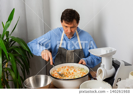 A 53-year-old man mixes cabbage and carrots in a large bowl in his kitchen while preparing for fermentation using simple tools and ingredients A 53-year-old man mixes cabbage and carrots in a large bowl in his kitchen while preparing for fermentation using simple tools and ingredients 140261988