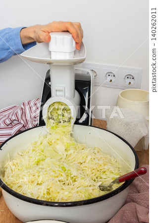 A 53-year-old man prepares cabbage and carrots for fermentation in his kitchen. He uses a machine to shred the vegetables while surrounded by kitchen tools and ingredients A 53-year-old man prepares cabbage and carrots for fermentation in his kitchen. He uses a machine to shred the vegetables while surrounded by kitchen tools and ingredients 140262011