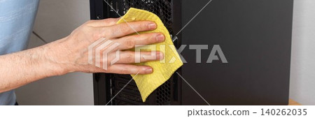 A 53-year-old man uses a cloth to clean dust from a computer system unit. He works at a wooden table in a room with plants nearby. Tools are set out for the task, banner A 53-year-old man uses a cloth to clean dust from a computer system unit. He works at a wooden table in a room with plants nearby. Tools are set out for the task, banner 140262035