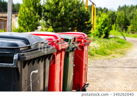 A Row of Colorful Waste Containers on a Sunny Day Surrounded by Lush Green Vegetation A Row of Colorful Waste Containers on a Sunny Day Surrounded by Lush Green Vegetation 140262040