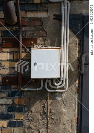 A Weathered Electrical Junction Box Mounted on a Rough Brick Wall Surrounded by Exposed Wires and Industrial Elements in Natural Lighting A Weathered Electrical Junction Box Mounted on a Rough Brick Wall Surrounded by Exposed Wires and Industrial Elements in Natural Lighting 140262041