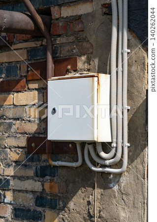A Detailed Look at an Old Electrical Junction Box Mounted on Weathered Brick Wall with Visible Wiring and Rust Accumulation 140262044