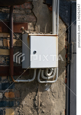 A Rusty Electrical Junction Box Mounted on a Brick Wall Surrounded by Exposed Wiring, Highlighting Urban Infrastructure and Its Aesthetic Decay A Rusty Electrical Junction Box Mounted on a Brick Wall Surrounded by Exposed Wiring, Highlighting Urban Infrastructure and Its Aesthetic Decay 140262047