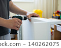 Person using cordless drill to assemble white furniture in bright indoor space with tools nearby 140262075