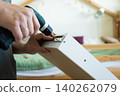Person using electric screwdriver to assemble furniture in a bright, modern bedroom setting 140262079