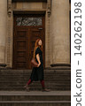 red-haired girl walks up steps with a bag in front of large building during late afternoon 140262198