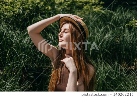 Woman sits on outdoor bench surrounded by green plants holding hand to straw hat. Managing urban heat stress, body hydration techniques , essential sun safe behaviors, summer fatigue prevention Woman sits on outdoor bench surrounded by green plants holding hand to straw hat. Managing urban heat stress, body hydration techniques , essential sun safe behaviors, summer fatigue prevention 140262215