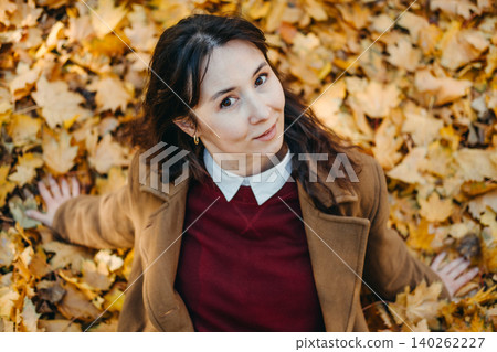 Woman sits on ground covered with autumn leaves looking up toward camera. Work life balance initiative, reducing workplace stress, corporate mental health awareness. Woman sits on ground covered with autumn leaves looking up toward camera. Work life balance initiative, reducing workplace stress, corporate mental health awareness. 140262227