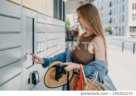 Woman uses automated parcel locker touchscreen while holding shopping bags on city street. Automated parcel locker pickup, modern post terminal delivery, smart parcel station interface. Woman uses automated parcel locker touchscreen while holding shopping bags on city street. Automated parcel locker pickup, modern post terminal delivery, smart parcel station interface. 140262233
