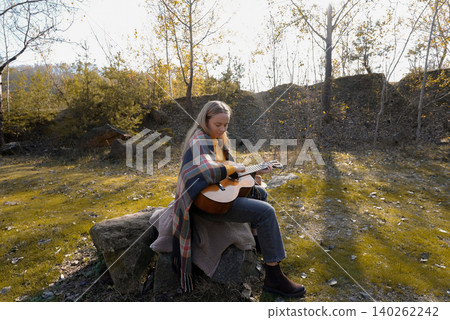 Blonde woman playing string guitar outdoors in autumn forest. Concept of sound therapy, mental health and wellness rituals. Calmness tranquility audio-sensory practices. Aura farming energy Blonde woman playing string guitar outdoors in autumn forest. Concept of sound therapy, mental health and wellness rituals. Calmness tranquility audio-sensory practices. Aura farming energy 140262242