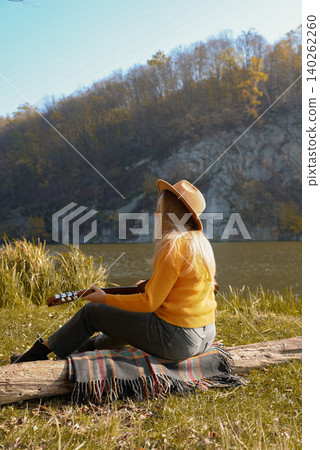 Blonde woman playing string guitar outdoors in autumn forest. Concept of sound therapy, mental health and wellness rituals. Calmness tranquility audio-sensory practices. Aura farming energy Blonde woman playing string guitar outdoors in autumn forest. Concept of sound therapy, mental health and wellness rituals. Calmness tranquility audio-sensory practices. Aura farming energy 140262260