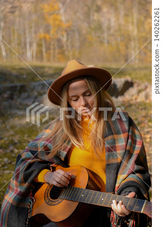 Blonde woman playing string guitar outdoors in autumn forest. Concept of sound therapy, mental health and wellness rituals. Calmness tranquility audio-sensory practices. Aura farming energy Blonde woman playing string guitar outdoors in autumn forest. Concept of sound therapy, mental health and wellness rituals. Calmness tranquility audio-sensory practices. Aura farming energy 140262261