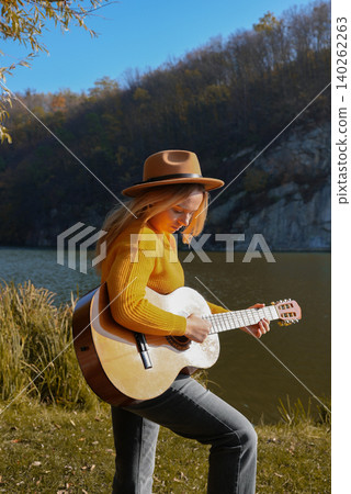 Blonde woman playing string guitar outdoors in autumn forest. Concept of sound therapy, mental health and wellness rituals. Calmness tranquility audio-sensory practices. Aura farming energy Blonde woman playing string guitar outdoors in autumn forest. Concept of sound therapy, mental health and wellness rituals. Calmness tranquility audio-sensory practices. Aura farming energy 140262263