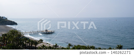 Waves crashing on wooden pier in Antalya Turkey. Palms and sea vacation travel tourism scene concept. Sandy beach and mountains Waves crashing on wooden pier in Antalya Turkey. Palms and sea vacation travel tourism scene concept. Sandy beach and mountains 140262271