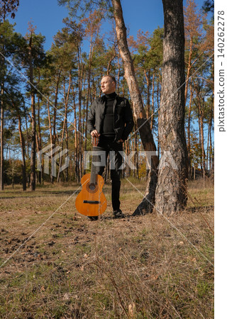 Portrait of smiling caucasian artist plays wooden acoustic guitar in autumnal park. Young songwriter plays string musical instrument hobby outside in nature fall time. Audio music healing 140262278