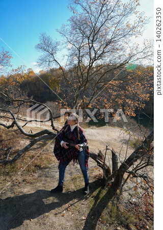 Portrait of smiling caucasian girl plays ukulele in autumnal park. Young woman plays guitar musical instrument outside in nature fall time. Audio music healing Portrait of smiling caucasian girl plays ukulele in autumnal park. Young woman plays guitar musical instrument outside in nature fall time. Audio music healing 140262350