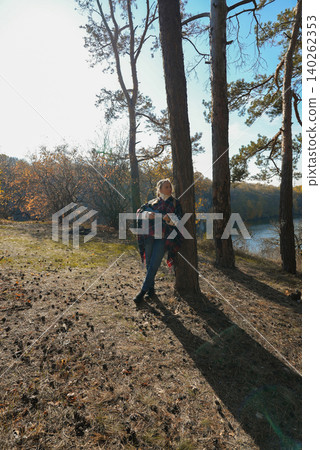 Beautiful blonde girl playing guitar ukulele and singing relaxing enjoying outdoors on sunny autumn day. Hippie woman in boho style training playing musical instrument. Fall leaves 140262353