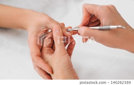 Beautician removing cuticle on female nails with special tool 140262389