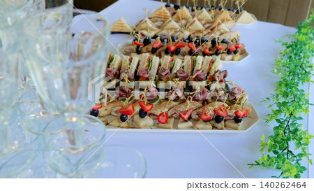 Elegant canapes with diverse toppings and empty wine glasses positioned on pristine white tablecloth, preparing for sophisticated catered gathering 140262464