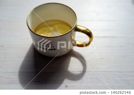 White ceramic mug with gold handle on sunlit wooden surface 140262548