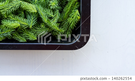 Green pine branches in black tray on white surface Green pine branches in black tray on white surface 140262554