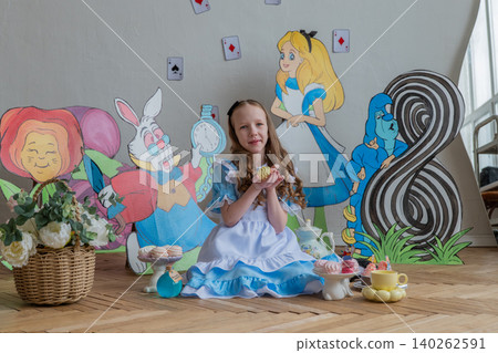 Little Caucasian Girl In Alice Dress Holding Toy Teacup, Surrounded By Cardboard Wonderland Cutouts, Wicker Basket With Flowers, Colorful Cupcakes On Wooden Floor, Soft Window Light, Playful Birthday Little Caucasian Girl In Alice Dress Holding Toy Teacup, Surrounded By Cardboard Wonderland Cutouts, Wicker Basket With Flowers, Colorful Cupcakes On Wooden Floor, Soft Window Light, Playful Birthday 140262591
