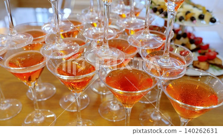 Martini glasses pyramided with orange aperol spritz, spilling over celebratory appetizers during festive party gathering Martini glasses pyramided with orange aperol spritz, spilling over celebratory appetizers during festive party gathering 140262631