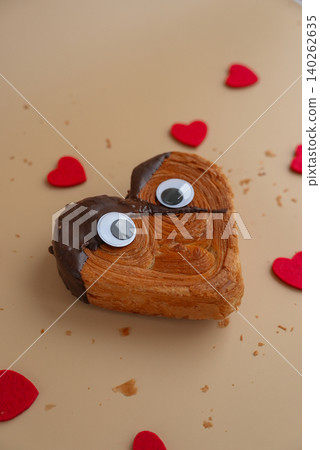 Funny creative eyes on Heart shaped dark chocolate croissant on beige background with copy space. Puff pastry new trendy sweet dessert bakery. Creamy dough Funny creative eyes on Heart shaped dark chocolate croissant on beige background with copy space. Puff pastry new trendy sweet dessert bakery. Creamy dough 140262635