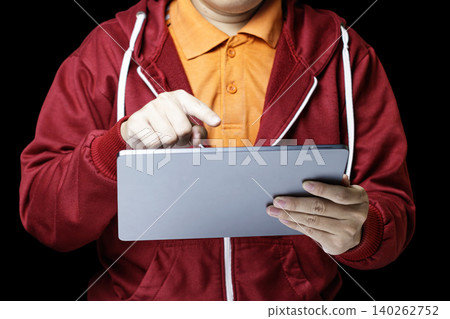 Person in red hoodie using a digital tablet. Finger taps screen with focused intent. Bright orange shirt contrasts dark background. Ideal for business, education. High quality photo 140262752