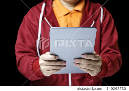 Person holds tablet with both hands. Red hoodie and orange shirt contrast starkly. Focused, calm demeanor suggests concentration. Ideal for tech, education, or remote work themes. High quality photo Person holds tablet with both hands. Red hoodie and orange shirt contrast starkly. Focused, calm demeanor suggests concentration. Ideal for tech, education, or remote work themes. High quality photo 140262780