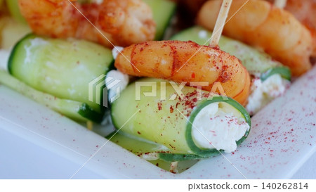 Cucumber rolls filled with creamy cheese, topped with grilled shrimp, sprinkled with paprika, serving elegant seafood appetizer on pristine plate 140262814