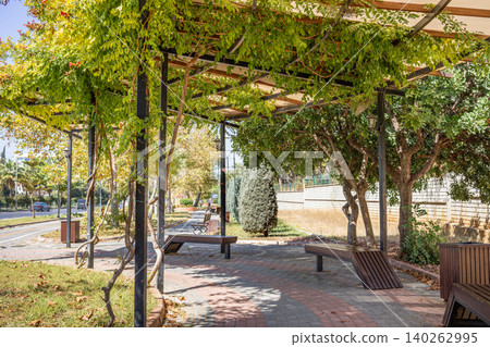 Park walkway with benches and green trellis structure in urban setting Park walkway with benches and green trellis structure in urban setting 140262995