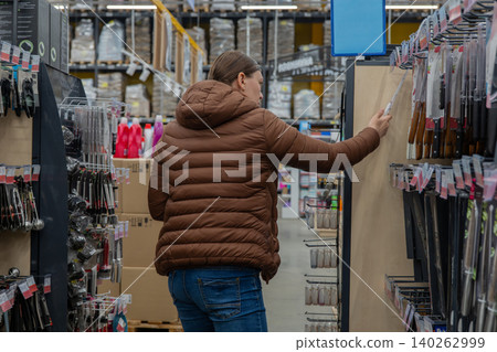 Woman Browsing Knives In Hardware Aisle, Meal Planner Comparing Blade Types, Brown Vest And Jeans, Packed Hook Displays, Fluorescent Lighting, Thoughtful Decision Making In Retail Environment Woman Browsing Knives In Hardware Aisle, Meal Planner Comparing Blade Types, Brown Vest And Jeans, Packed Hook Displays, Fluorescent Lighting, Thoughtful Decision Making In Retail Environment 140262999