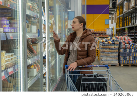 Lady browsing frozen meals peacefully. Caucasian woman calmly exploring prepackaged foods. Caucasian woman is calmly shopping and inspecting various frozen food choices during peaceful evening Lady browsing frozen meals peacefully. Caucasian woman calmly exploring prepackaged foods. Caucasian woman is calmly shopping and inspecting various frozen food choices during peaceful evening 140263063