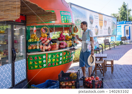 Man selects fresh fruits at colorful outdoor fruit stand in market Man selects fresh fruits at colorful outdoor fruit stand in market 140263102