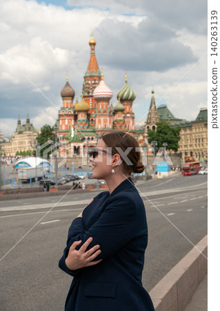 Woman in dark blazer stands near Saint Basil's Cathedral in Moscow, with iconic colorful domes and Red Square surroundings, cultural travel scene. Moscow tourism, travel, city branding 140263139