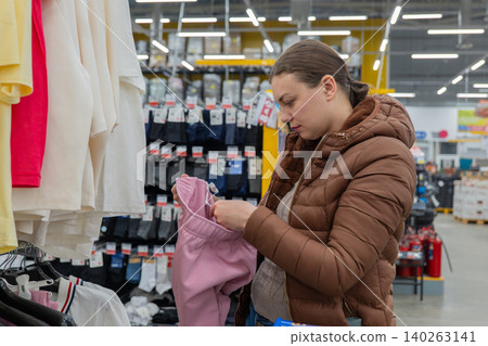 Woman Holding Pink Home Pants Near Rack, Prioritizing Comfort And Budget, Comparing Sizes And Elastic Waist, Preparing Cozy Wardrobe For Weekend, Fluorescent Supermarket Atmosphere, Focused Shopper Woman Holding Pink Home Pants Near Rack, Prioritizing Comfort And Budget, Comparing Sizes And Elastic Waist, Preparing Cozy Wardrobe For Weekend, Fluorescent Supermarket Atmosphere, Focused Shopper 140263141