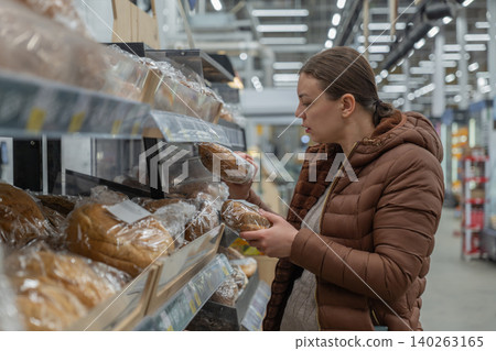 Woman reviews product content. Woman thoughtfully examines packaging for additives and preservatives. Careful customer evaluates list of ingredients before making purchase decision in supermarket Woman reviews product content. Woman thoughtfully examines packaging for additives and preservatives. Careful customer evaluates list of ingredients before making purchase decision in supermarket 140263165