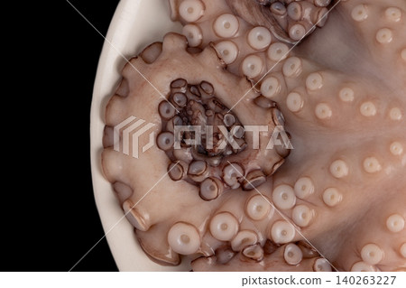Raw octopus, a popular seafood delicacy, displaying its textured tentacles and numerous suction cups, ready for culinary preparation against a dark background Raw octopus, a popular seafood delicacy, displaying its textured tentacles and numerous suction cups, ready for culinary preparation against a dark background 140263227