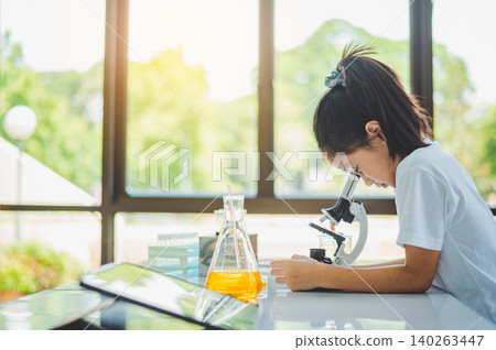 little scientist looking through a microscope and test tubes filled with chemicals for learning about science and experiments. little scientist looking through a microscope and test tubes filled with chemicals for learning about science and experiments. 140263447