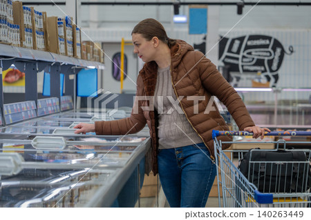 Woman Checking Prices In Supermarket Aisle, Comparing Brands And Scanning Tags, Practical Posture With Cart, Everyday Outfit, Budgetminded Grocery Run Atmosphere With Visible Shelf Signage. Woman Checking Prices In Supermarket Aisle, Comparing Brands And Scanning Tags, Practical Posture With Cart, Everyday Outfit, Budgetminded Grocery Run Atmosphere With Visible Shelf Signage. 140263449