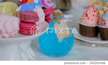 Pastel Dessert Display With Macarons, Bottle Softfocus Tabletop Scene With Macarons On White Cake Stand, Blue Corked Bottle With Blank Tag, Cupcakes With Pink Frosting, Airy Bokeh Background, Styled Pastel Dessert Display With Macarons, Bottle Softfocus Tabletop Scene With Macarons On White Cake Stand, Blue Corked Bottle With Blank Tag, Cupcakes With Pink Frosting, Airy Bokeh Background, Styled 140263486