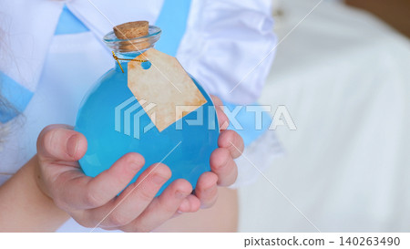 Child Hands Holding Blue Bottle With Cork And Blank Tag, Closeup Shot In Soft Natural Light, Minimalist Background, Handmade Bath Oil Gift Suggesting Gentle Spa Ritual, Apothecary Play In Childhood, 140263490