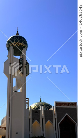 Mosque minaret rises beside patterned domes under brilliant blue sky, mosque detail expressing sacred geometry, crisp light, and travel destination appeal for cultural architecture collections. 140263548