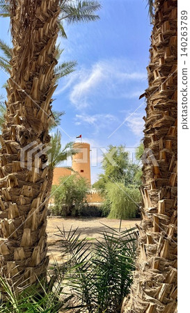 Twin Palms Framing Distant Minaret Tower, Sandy Ground And Shadowed Trunks, Clear Blue Sky, Heritage Architecture Offering Hidden Skyline View And Serene Cultural Perspective Twin Palms Framing Distant Minaret Tower, Sandy Ground And Shadowed Trunks, Clear Blue Sky, Heritage Architecture Offering Hidden Skyline View And Serene Cultural Perspective 140263789