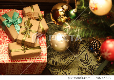 Top view of wrapped Christmas gift boxes under a decorated Christmas tree. Holiday presents in craft paper with ribbons next to festive baubles and ornaments Top view of wrapped Christmas gift boxes under a decorated Christmas tree. Holiday presents in craft paper with ribbons next to festive baubles and ornaments 140263829