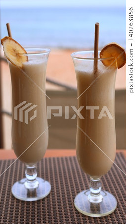 Refreshing Tropical Banana Beverage In Sunlight. Enjoy Cool Banana Smoothie With Ocean View Backdrop. Tropical Banana Smoothies In Tall Glasses With Ocean And Sunlight Ambiance Refreshing Tropical Banana Beverage In Sunlight. Enjoy Cool Banana Smoothie With Ocean View Backdrop. Tropical Banana Smoothies In Tall Glasses With Ocean And Sunlight Ambiance 140263856
