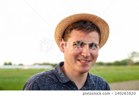 Portrait of a smiling young man in a straw hat outdoors. Close-up of a handsome happy guy looking at the camera in a green field background at sunset Portrait of a smiling young man in a straw hat outdoors. Close-up of a handsome happy guy looking at the camera in a green field background at sunset 140263920