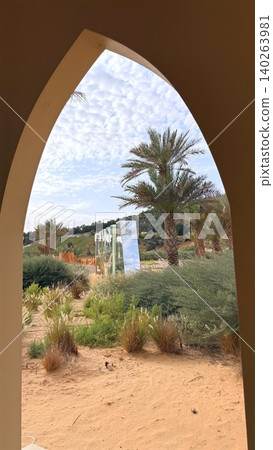 Arched Window Over Desert Oasis. Serene Courtyard Scene With Palm Trees And Bright Sky. Tranquil Desert Landscape Seen Through Elegant Arched Window With Palms And Sunlight Arched Window Over Desert Oasis. Serene Courtyard Scene With Palm Trees And Bright Sky. Tranquil Desert Landscape Seen Through Elegant Arched Window With Palms And Sunlight 140263981