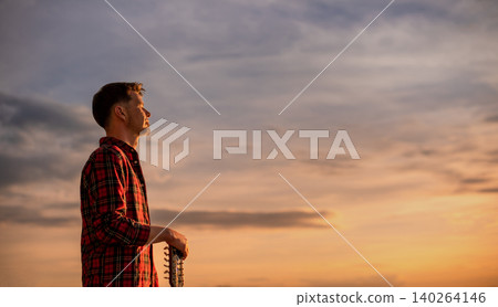 Male Musician Holding Acoustic Guitar at Sunset Sky Male Musician Holding Acoustic Guitar at Sunset Sky 140264146